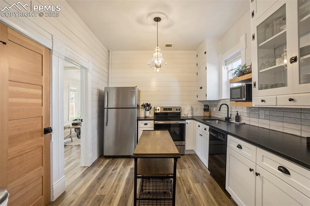 Kitchen with white cabinets, stainless steel appliances, light wood-style flooring, dark countertops, and hanging light fixtures