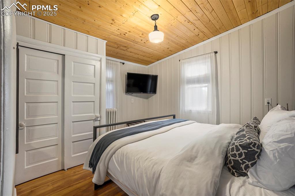 Bedroom with wood finished floors, ornamental molding, a closet, and wood ceiling
