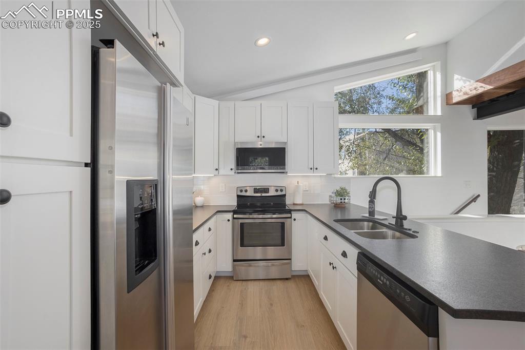 Kitchen featuring a peninsula, appliances with stainless steel finishes, lofted ceiling, dark countertops, and white cabinets