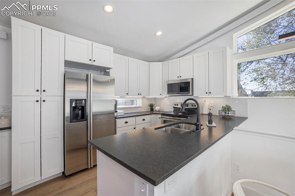 Kitchen featuring stainless steel appliances, white cabinetry, decorative backsplash, a peninsula, and light wood-type flooring