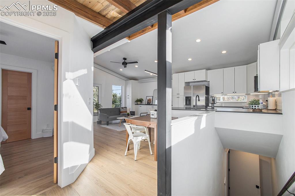 Kitchen featuring white cabinets, beam ceiling, ceiling fan, light wood-type flooring, and stainless steel fridge with ice dispenser