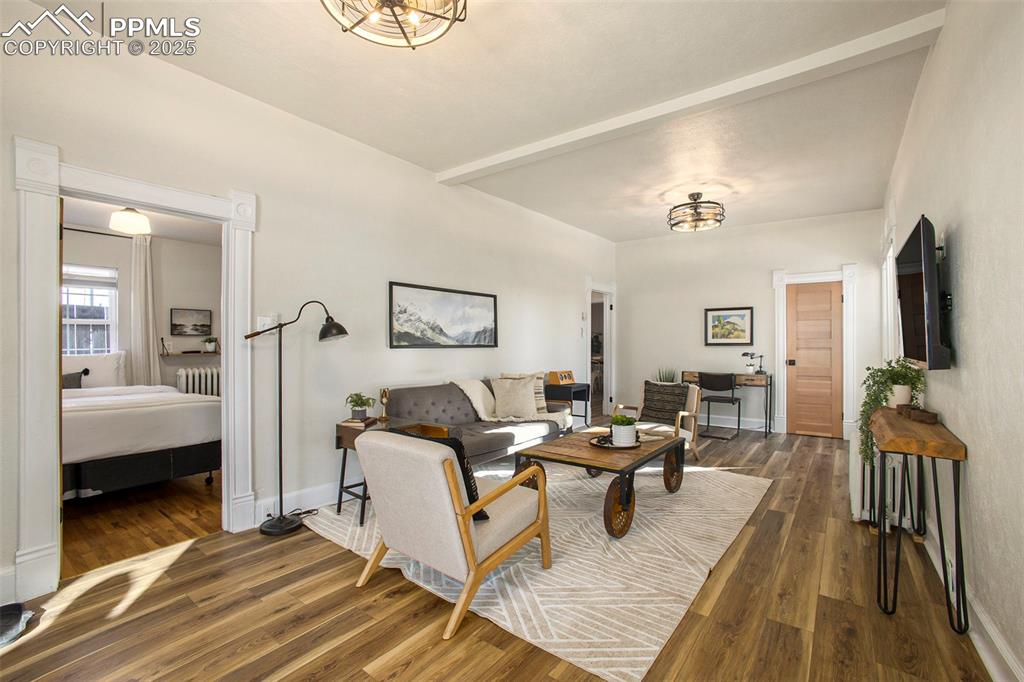 Living room with dark wood-style flooring, beamed ceiling, radiator heating unit, and a chandelier