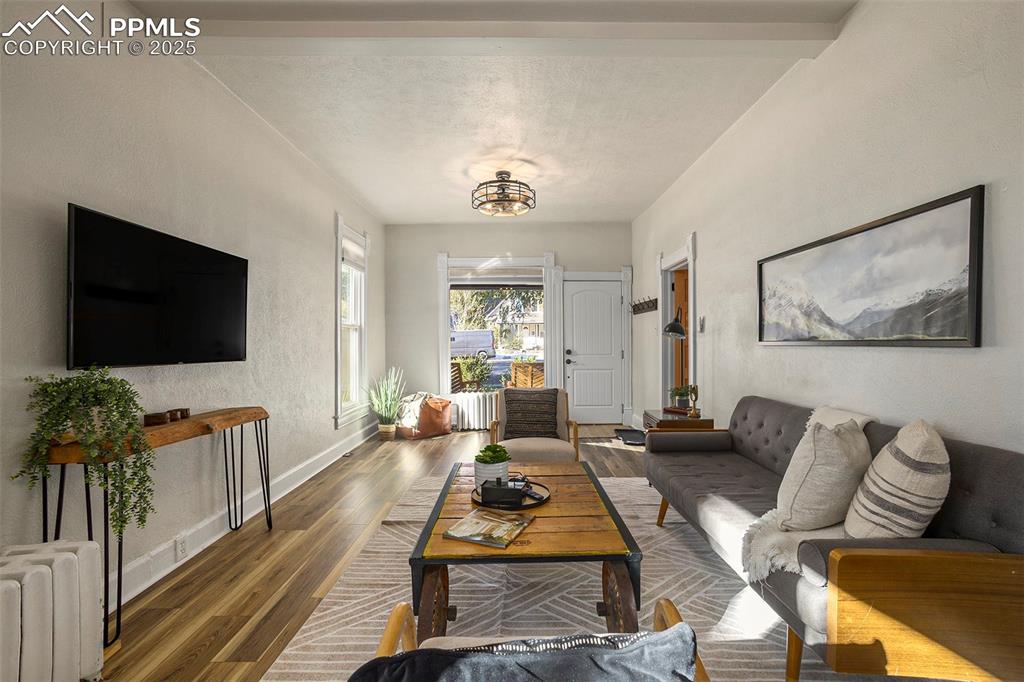Living room featuring wood finished floors, beamed ceiling, a textured wall, and radiator heating unit