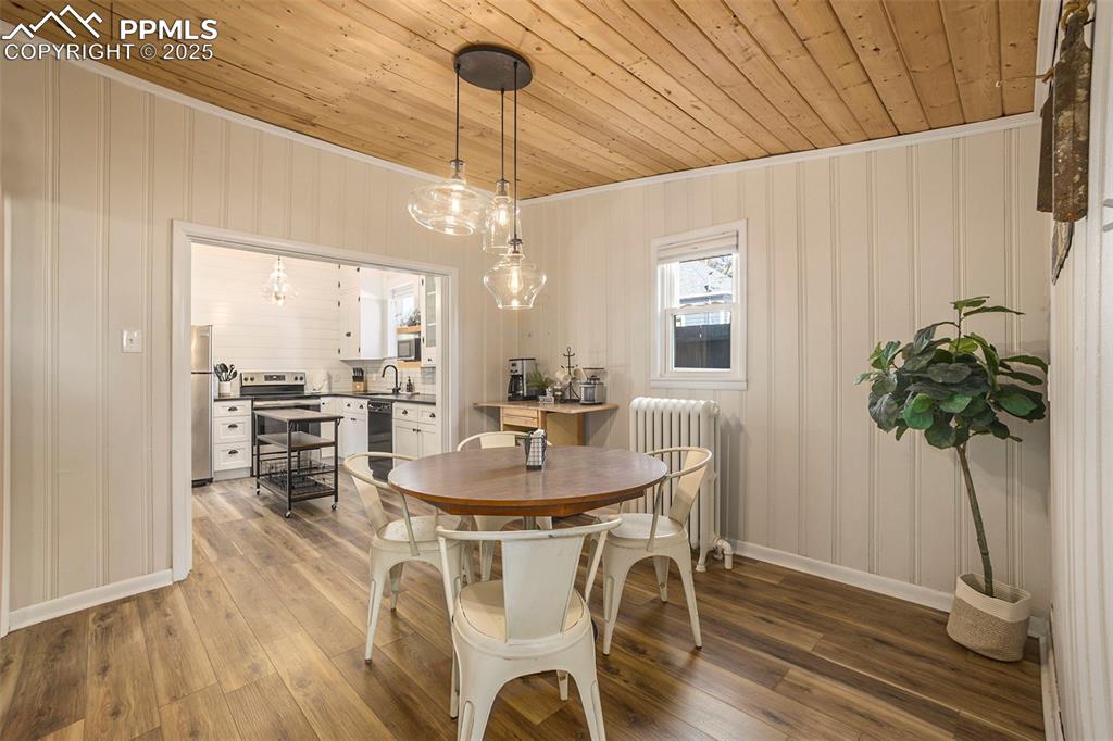 Dining room with radiator heating unit, wood ceiling, light wood finished floors, and crown molding