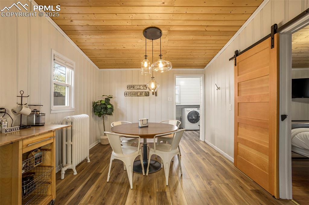 Dining space with a barn door, radiator, wood ceiling, crown molding, and wood finished floors