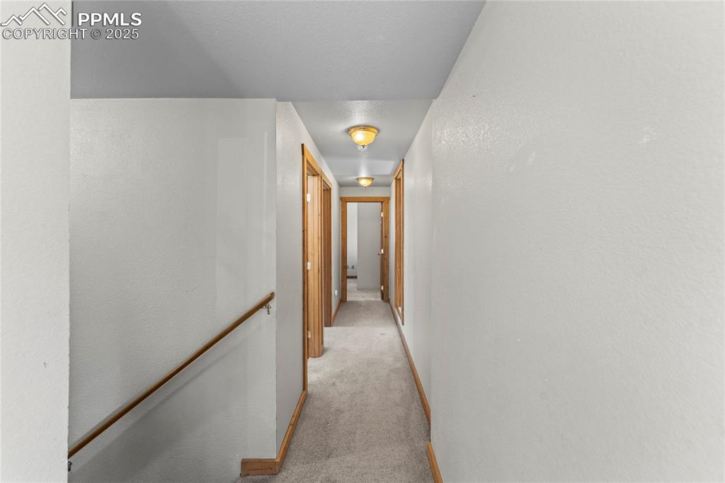 Hallway with light colored carpet and an upstairs landing