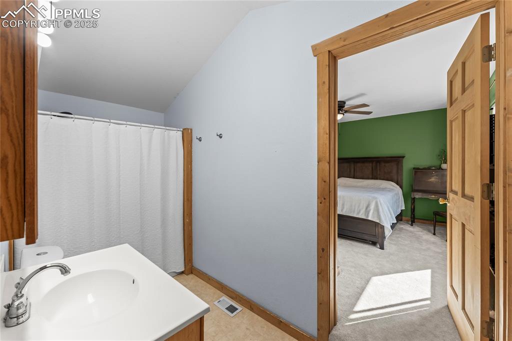 Full bath featuring lofted ceiling, vanity and master bedroom