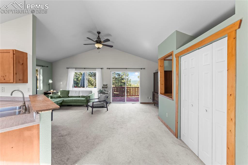 Front entry into living area with light colored carpet, a ceiling fan, and vaulted ceiling