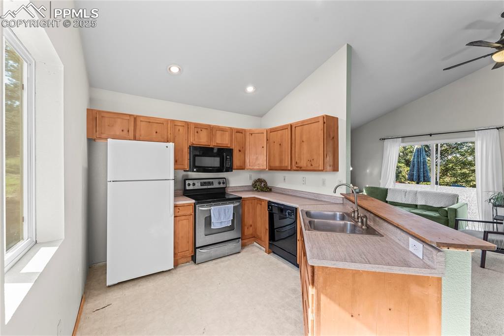 Kitchen featuring a peninsula, black appliances, light countertops, light flooring, and lofted ceiling