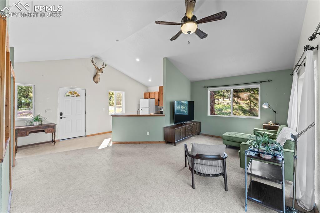 Living area with light carpet, ceiling fan, and high vaulted ceiling