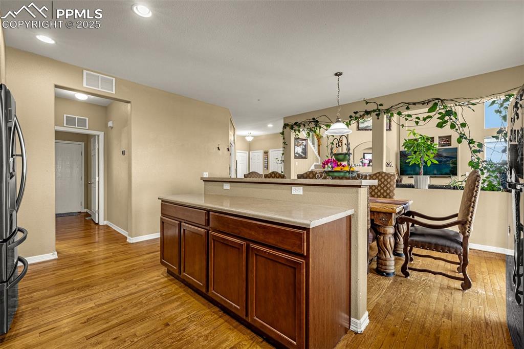 Kitchen with decorative light fixtures, light wood-style floors, stainless steel fridge with ice dispenser, recessed lighting, and light countertops