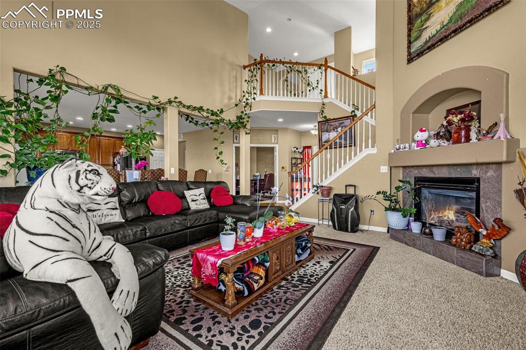 Carpeted living area featuring a fireplace, recessed lighting, stairway, and a high ceiling