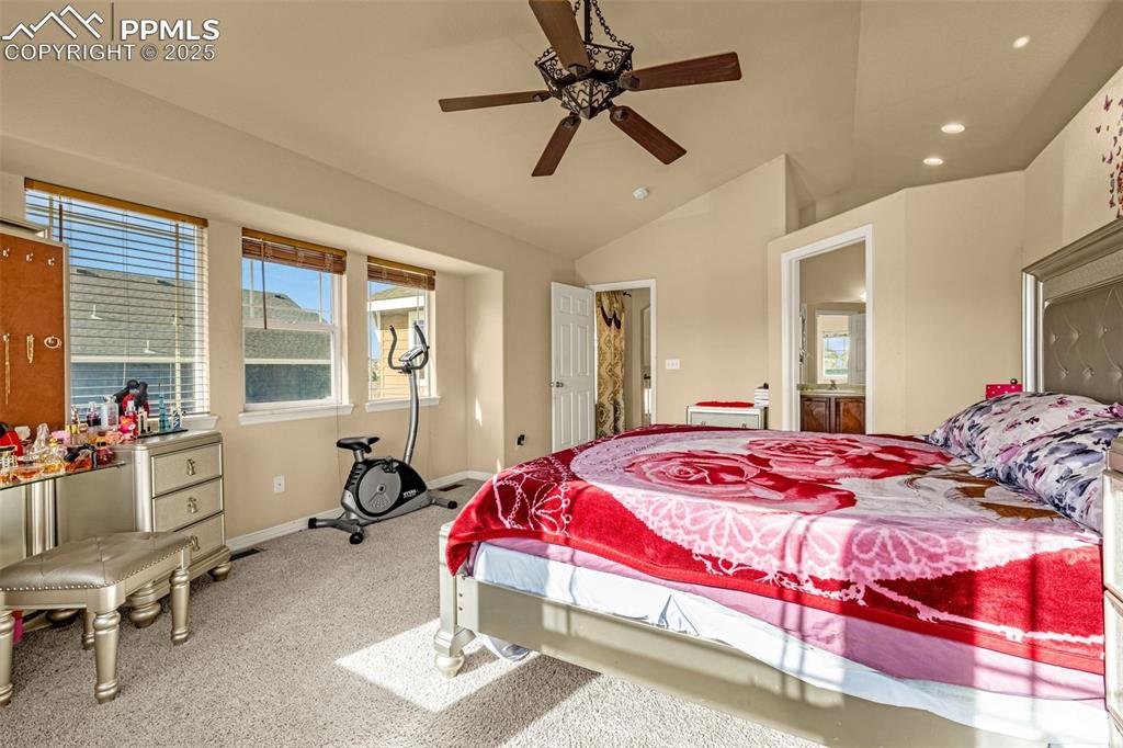 Carpeted bedroom featuring lofted ceiling, recessed lighting, ceiling fan, and ensuite bath