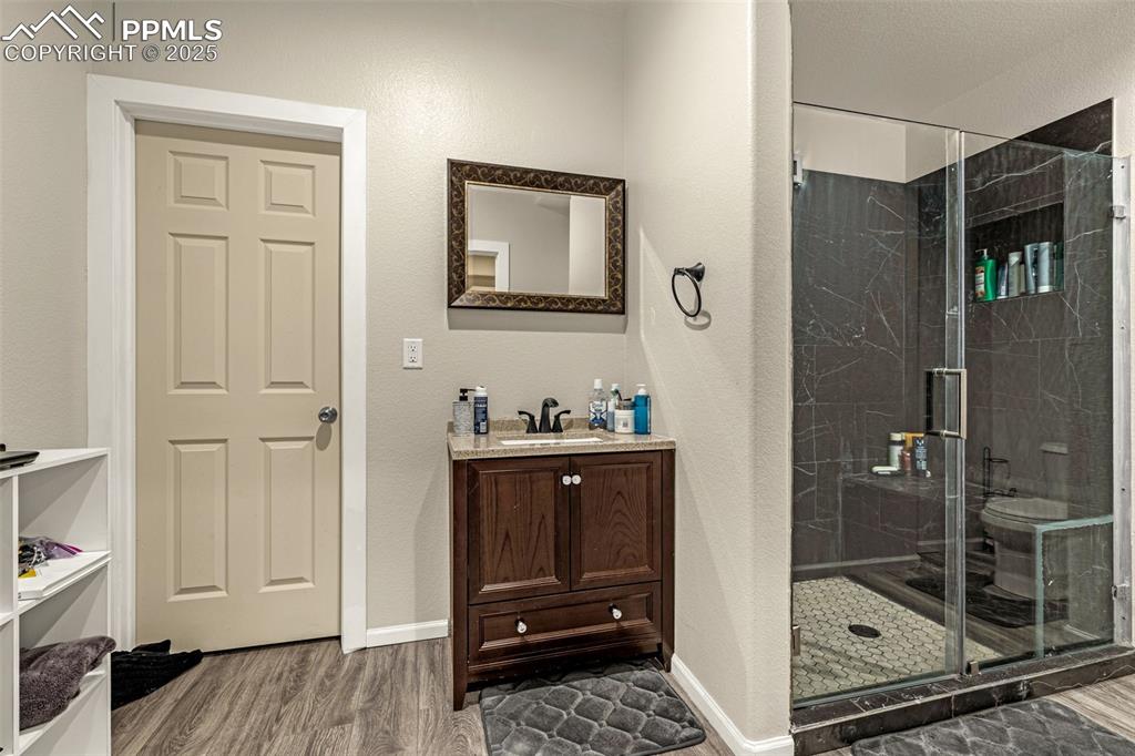 Bathroom with vanity, a marble finish shower, dark wood-style flooring, and a textured wall
