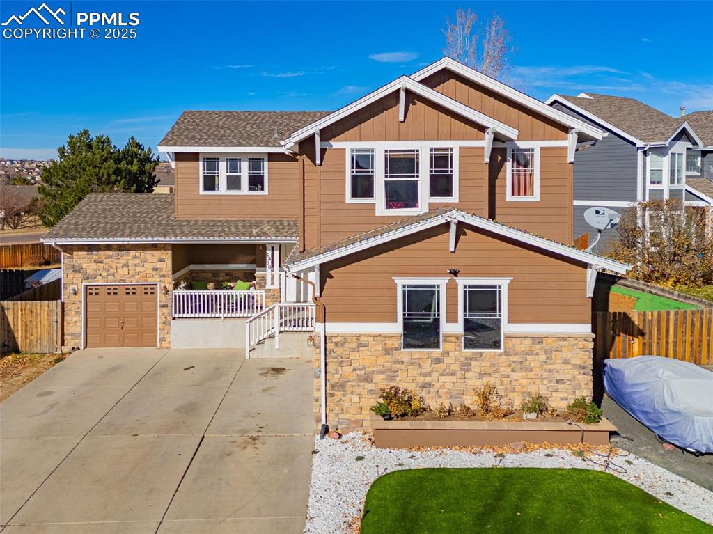 Craftsman inspired home featuring stone siding, driveway, board and batten siding, and roof with shingles