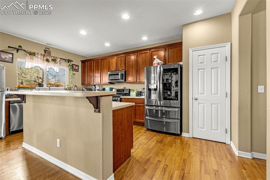 Kitchen featuring light countertops, stainless steel appliances, brown cabinets, light wood-style flooring, and recessed lighting