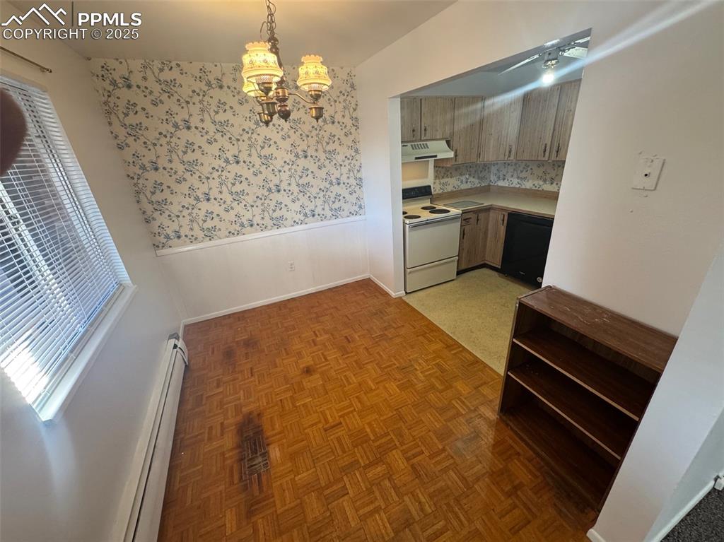 Kitchen featuring a wainscoted wall, a baseboard radiator, electric range, light countertops, and decorative light fixtures