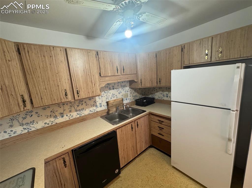 Kitchen with freestanding refrigerator, black dishwasher, light countertops, and ceiling fan