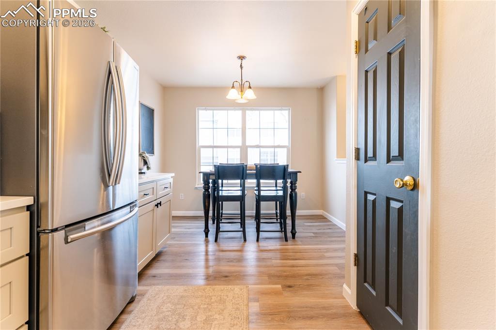 Kitchen with freestanding refrigerator, light wood finished floors, hanging lights, and white cabinets