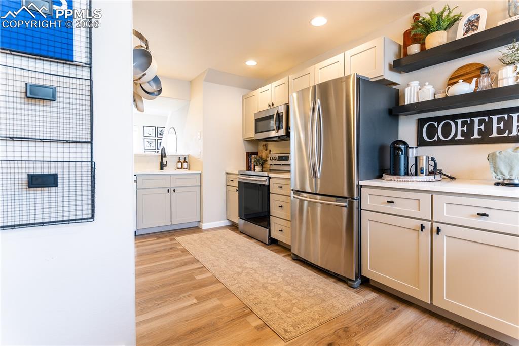 Kitchen with stainless steel appliances, open shelves, light wood-style flooring, and recessed lighting