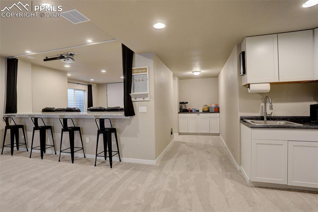 Lower level/basement living area featuring recessed lighting and large windows. Wet bar/kitchen, cabinetry, theater counter for snacks and more cabinets. Stone top bar for eating, crafting, watching movies.