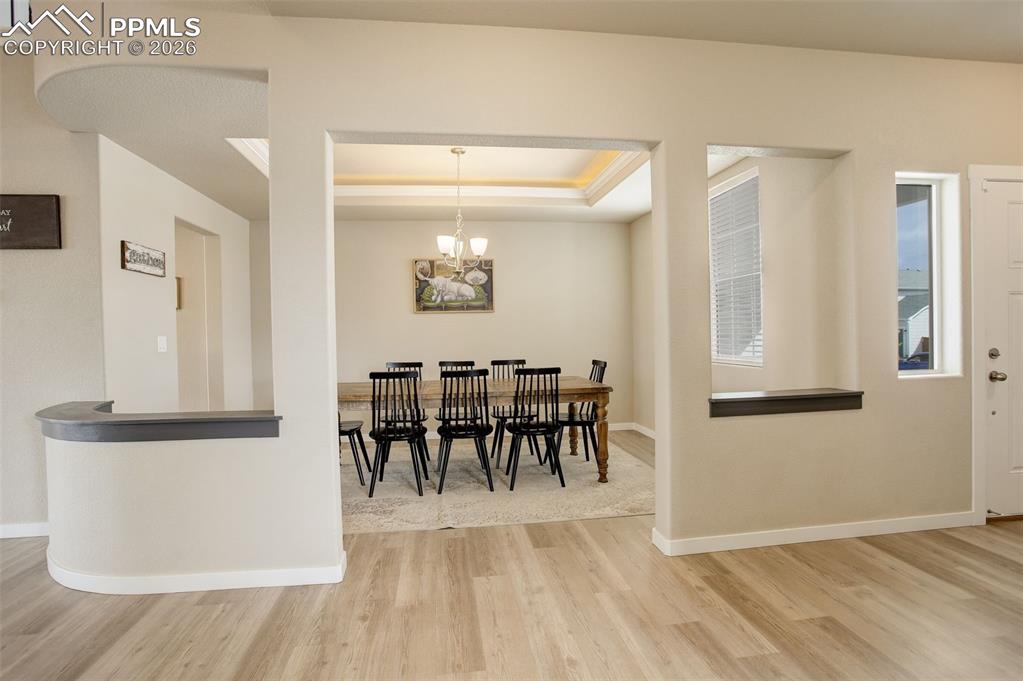 Dining area featuring light wood-style floors, a chandelier, and a raised ceiling