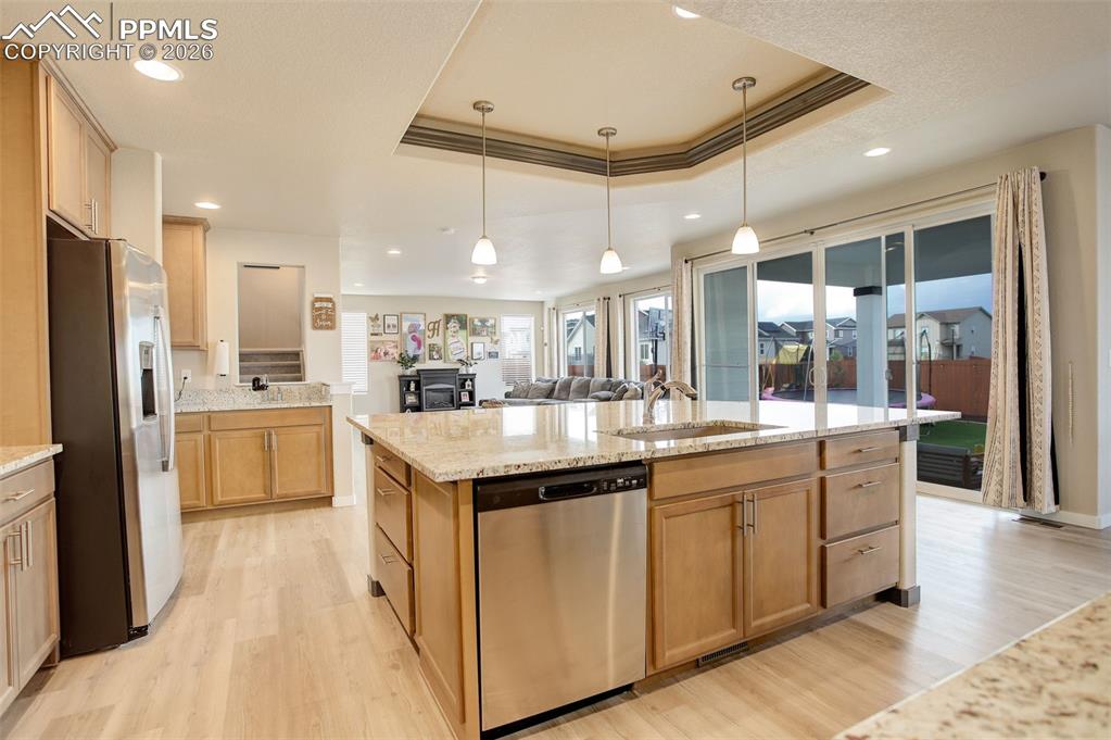 Kitchen with stainless steel appliances, a raised ceiling, a kitchen breakfast bar, light stone counters, and a center island with sink.
