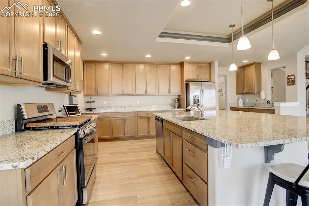 Kitchen featuring stainless steel refrigerator with ice dispenser, light stone counters, wood finish cabinetry, light wood finished floors, and a tray ceiling