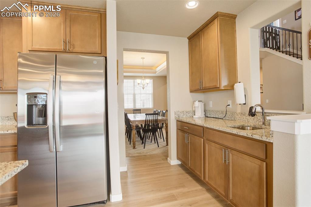 Kitchen featuring stainless steel refrigerator with ice dispenser, light stone counters, wood finish cabinetry, light wood finished floors, and a tray ceiling, coffee bar, or wet bar with sink, prep sink and additional cabinets.