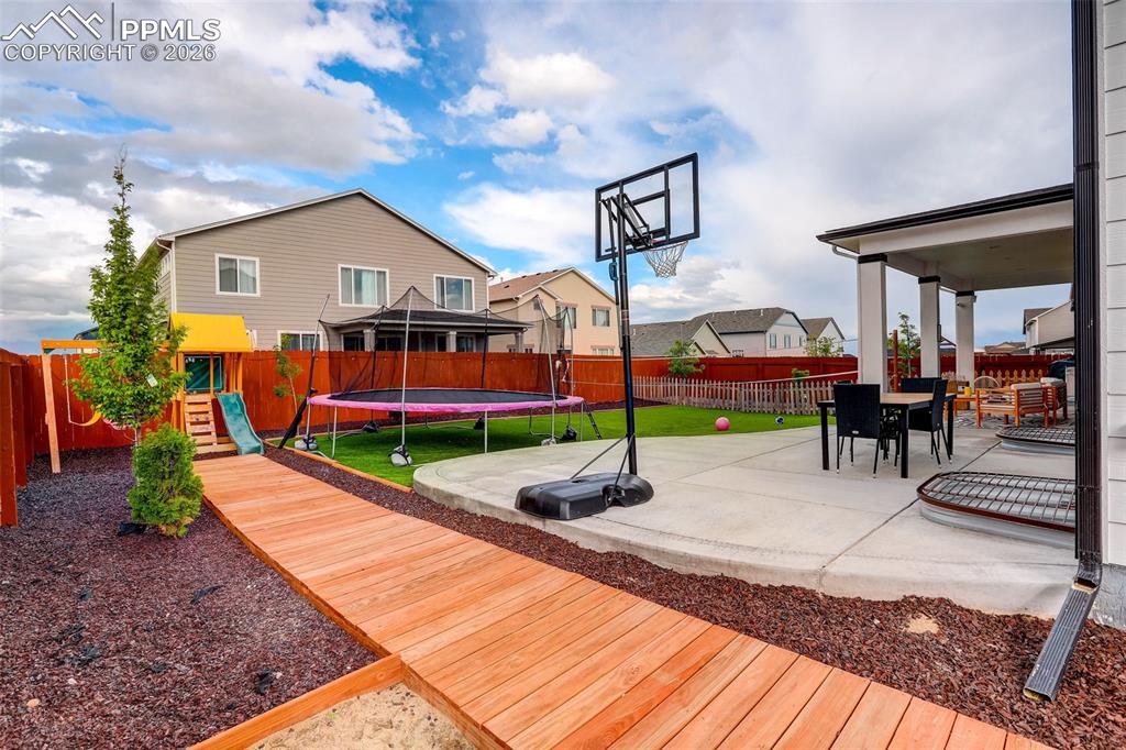 Deck with a playground, a trampoline, a patio, and a fenced backyard