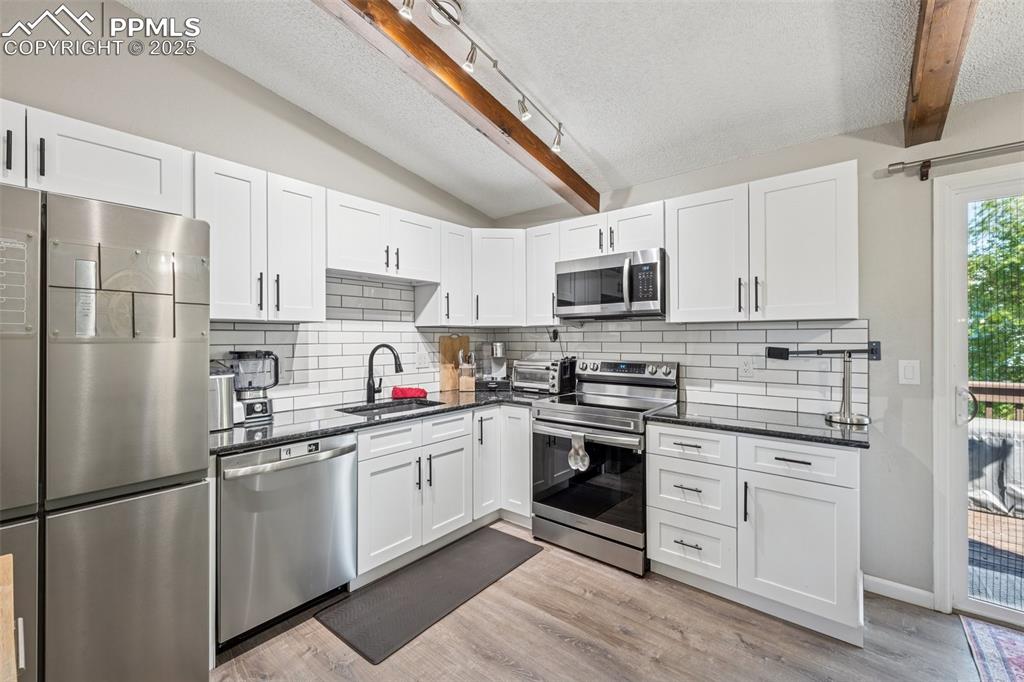 Kitchen featuring a textured ceiling, appliances with stainless steel finishes, white cabinets, and dark stone counters