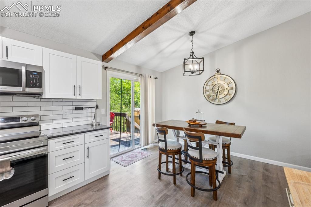 Kitchen featuring stainless steel appliances, white cabinets, hanging light fixtures, dark wood-type flooring, and backsplash
