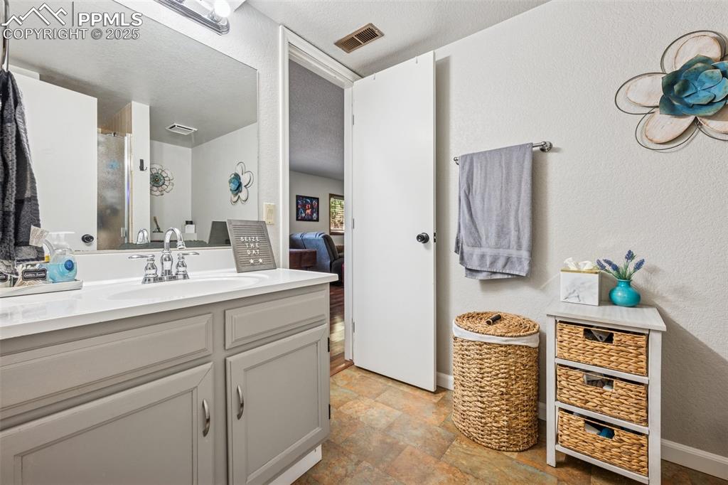 Ensuite bathroom with vanity, a textured wall, a shower stall, stone finish flooring, and a textured ceiling