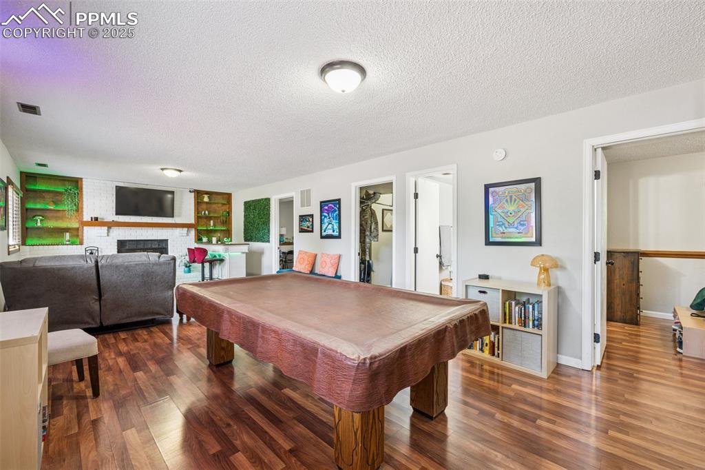 Rec room featuring billiards, a textured ceiling, dark wood finished floors, and a brick fireplace