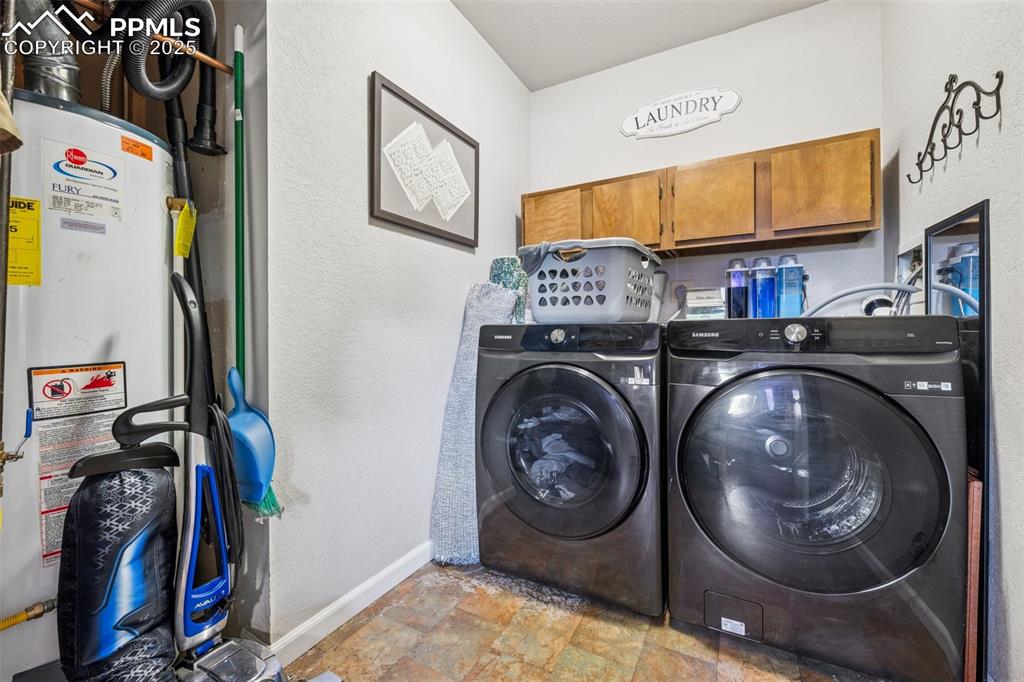 Laundry room featuring a textured wall, stone finish flooring, gas water heater, and washing machine and clothes dryer