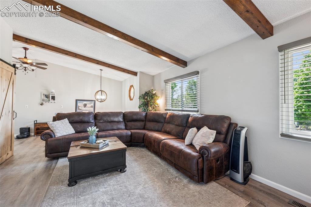 Living room featuring a textured ceiling, wood finished floors, ceiling fan, a barn door, and a chandelier