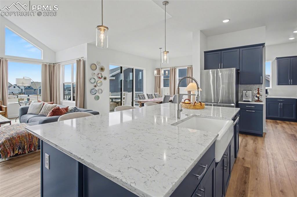 Kitchen with light wood-style flooring, open floor plan, blue cabinetry, hanging light fixtures, and vaulted ceiling