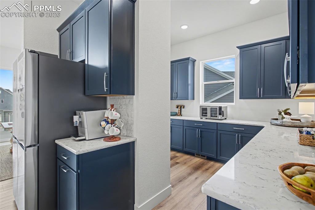 Kitchen featuring blue cabinetry, light stone countertops, and light wood-type flooring