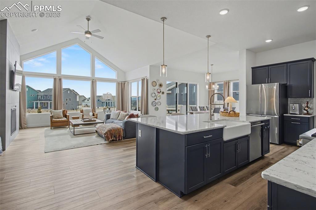 Kitchen featuring open floor plan, a ceiling fan, light stone counters, stainless steel appliances, and a high ceiling