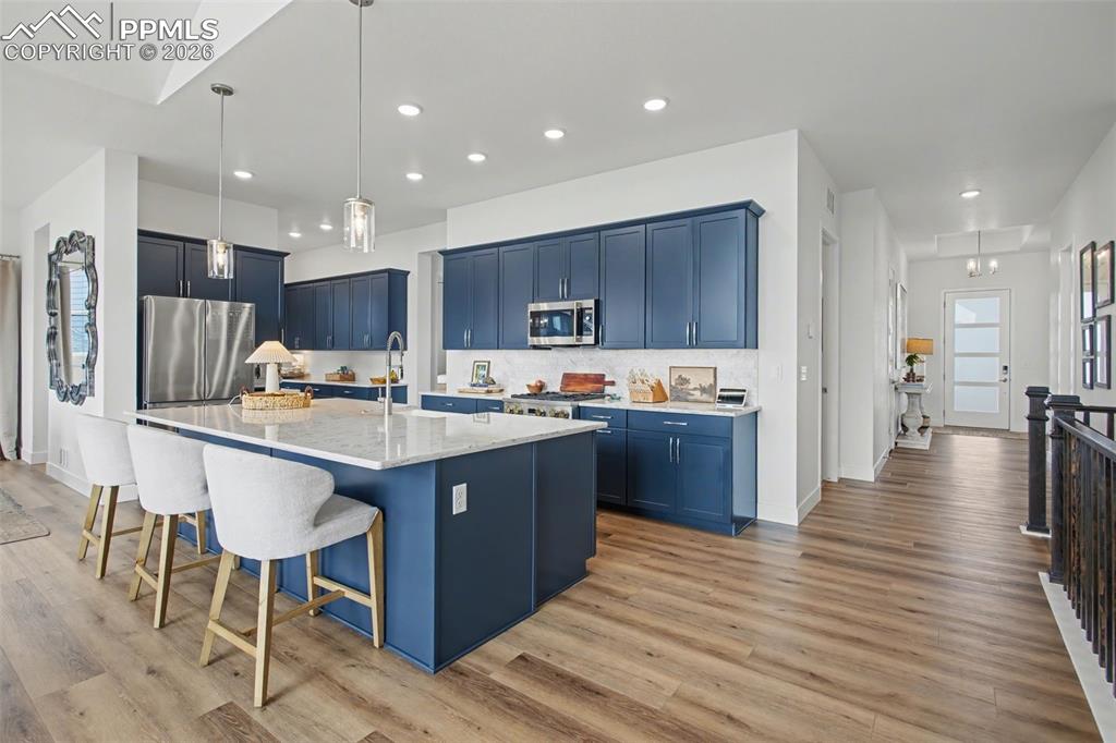Kitchen featuring a center island with sink, a kitchen bar, light stone counters, stainless steel appliances, and decorative light fixtures