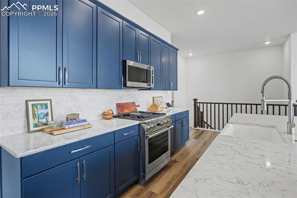 Kitchen featuring blue cabinets, stainless steel appliances, light stone counters, light wood-style flooring, and decorative backsplash