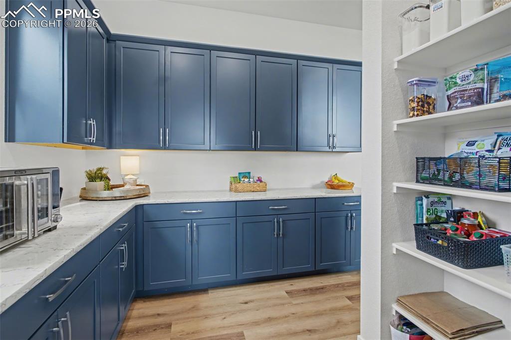 Kitchen with blue cabinets, light wood-style floors, and light stone counters