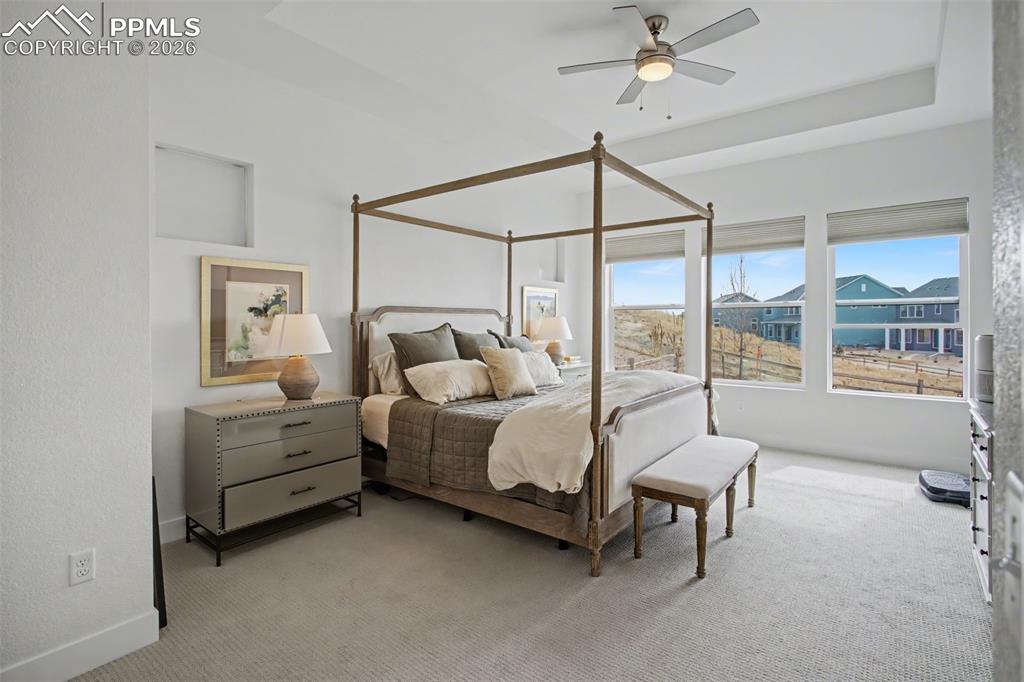 Bedroom with light colored carpet, a ceiling fan, and a tray ceiling