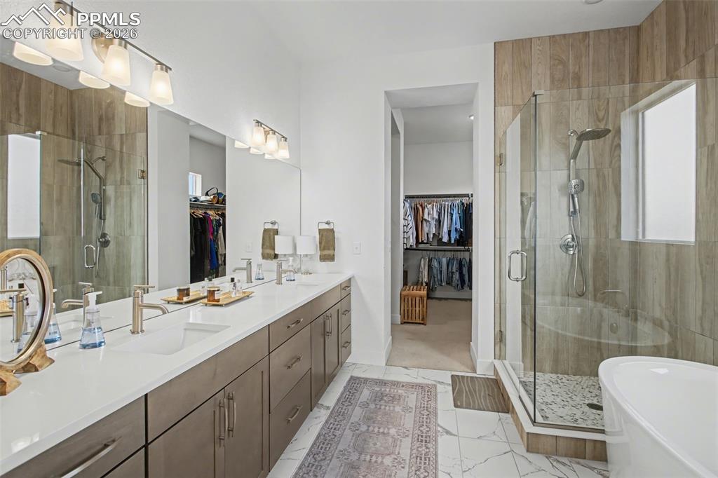 Full bathroom featuring a spacious closet, a shower stall, double vanity, and a freestanding tub