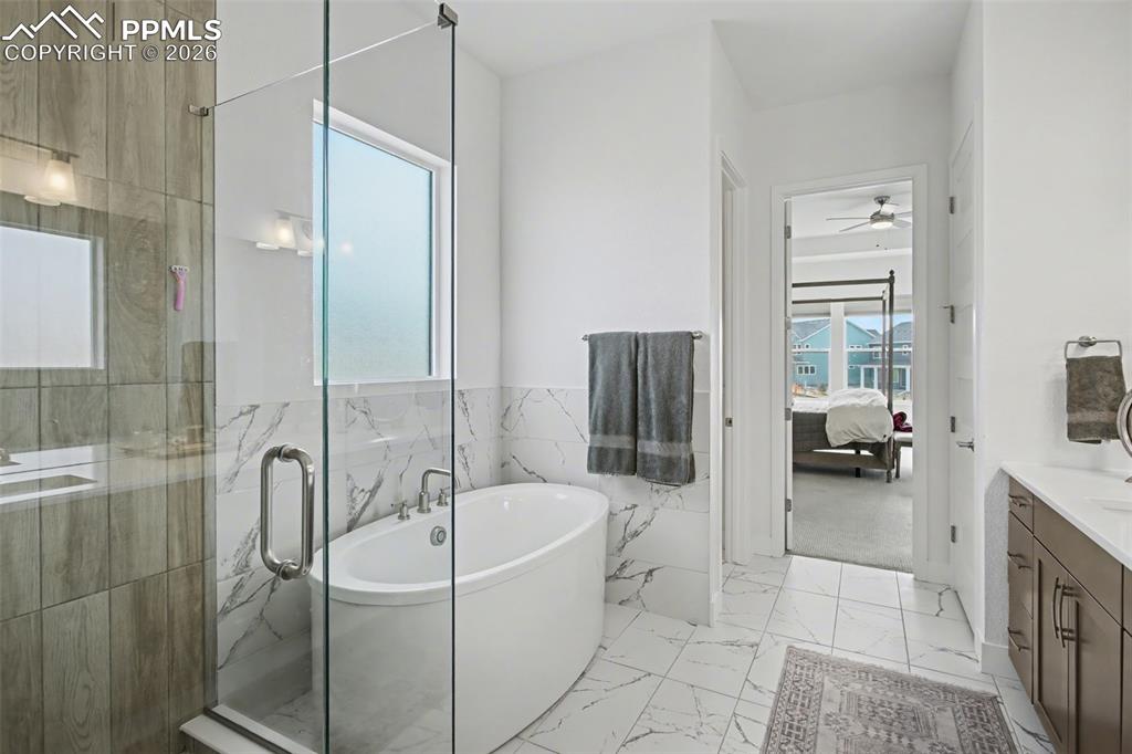 Ensuite bathroom with vanity, a soaking tub, a marble finish shower, light marble finish floors, and wainscoting