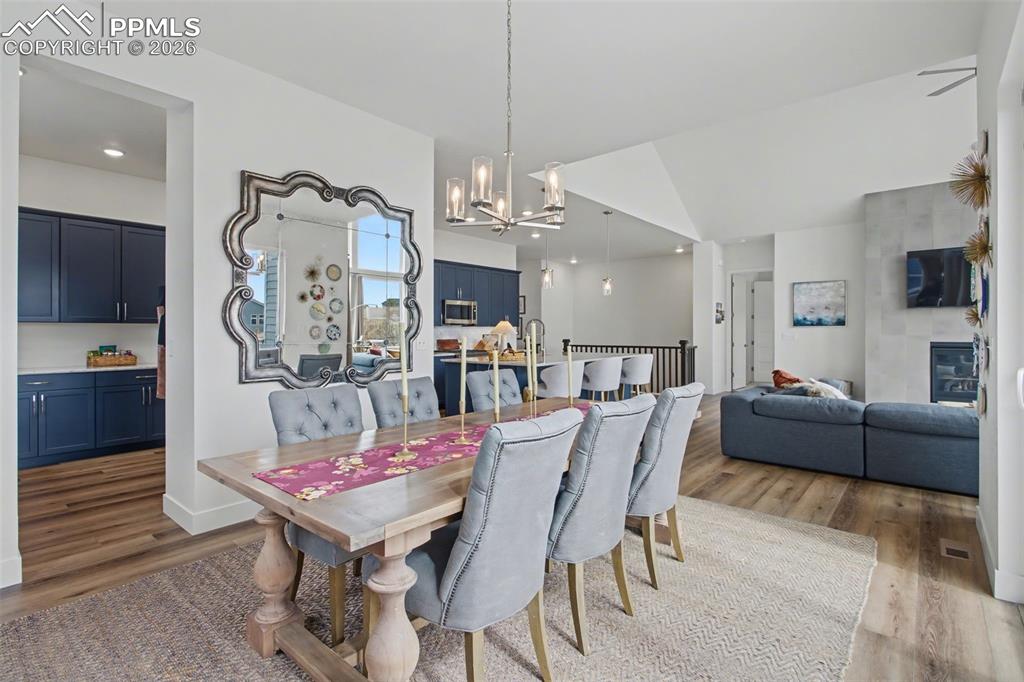 Dining room with light wood-style floors, hanging lights, and vaulted ceiling