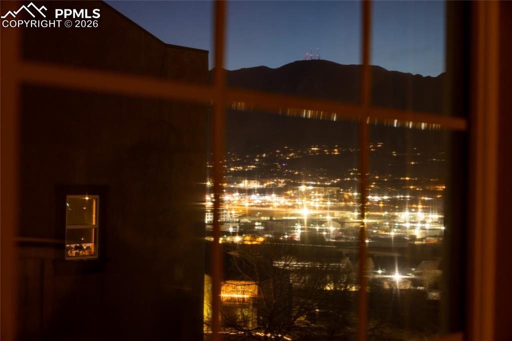 City and mountain night view from upper bedroom — twinkling city lights below.
