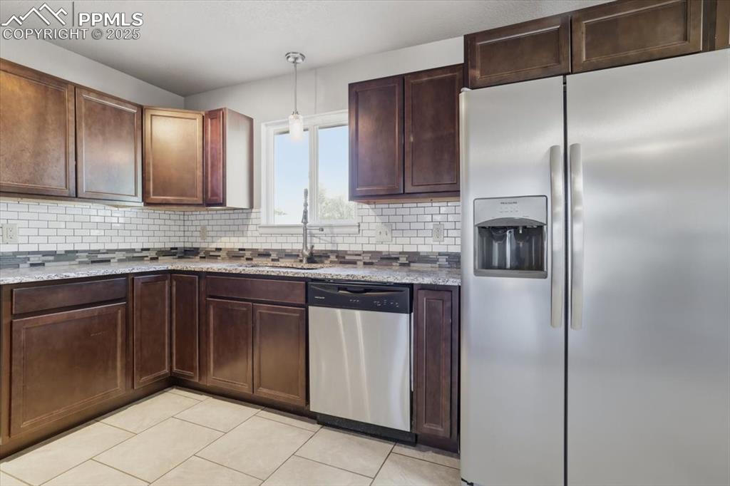 Kitchen featuring appliances with stainless steel finishes, hanging light fixtures, light tile patterned floors, tasteful backsplash, and light stone countertops