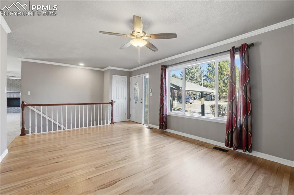 Unfurnished room with crown molding, light wood-style flooring, ceiling fan, and a textured ceiling