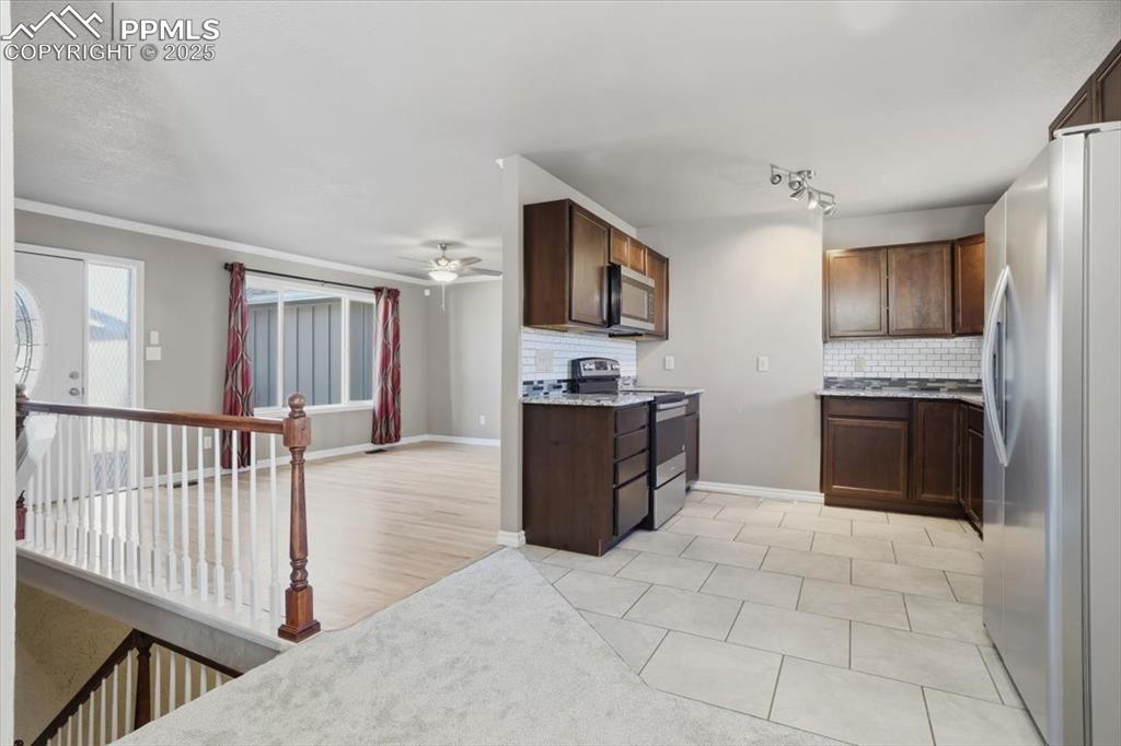 Kitchen with stainless steel appliances, decorative backsplash, light tile patterned floors, and dark brown cabinets
